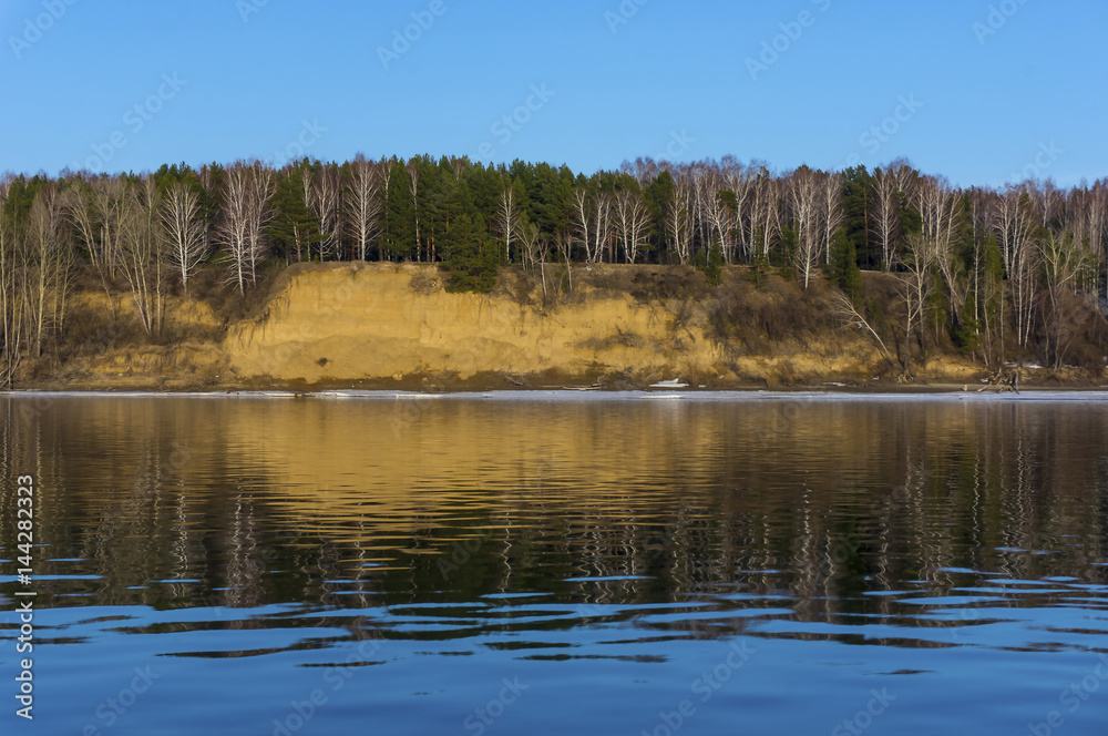 The steep bank of the river is reflected in the water surface of the river. Beautiful reflection of the shore in the water.