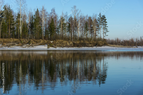 Island in the snow reflected in the water. Spring landscape on the bank of the river Ob.