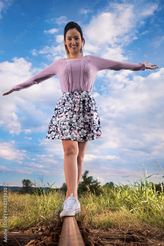 Cheerful young woman with outstretched arms is walking on railroad track Cheerful young woman with outstretched arms is walking on railroad track