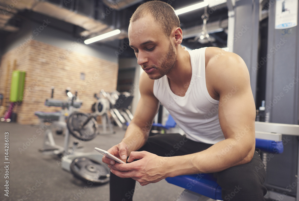 Muscular young man using cell phone at gym . Muscular young man using cell phone at gym .