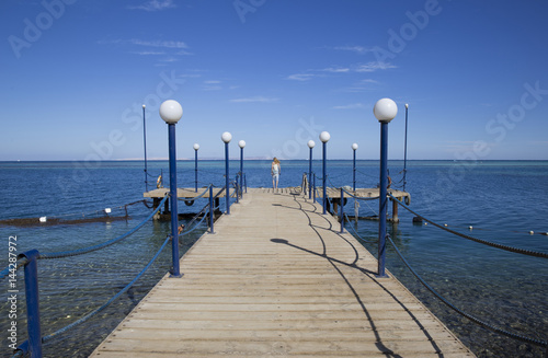 Away on a wooden pier a young girl with long blond hair by the sea