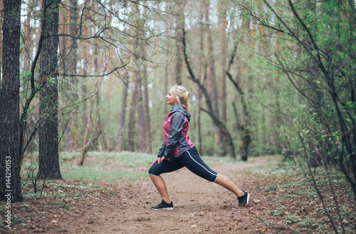 young beautiful girl doing workout in the woods. Blonde girl tracksuit doing exercises