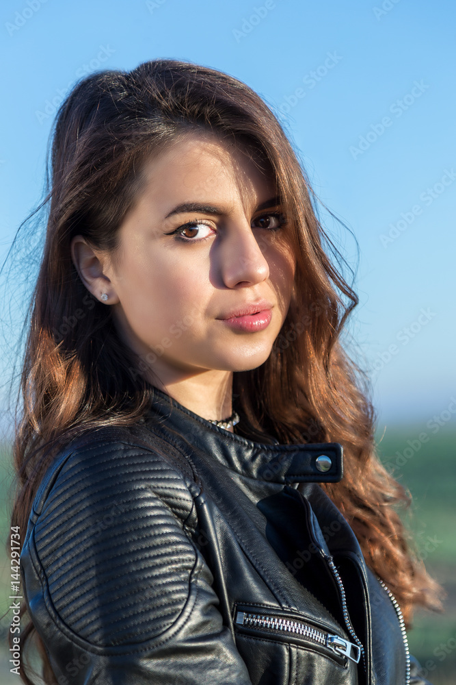 Fototapeta premium Portrait of sweet brunette girl in leather jacket looking at the camera