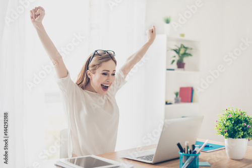 Yes! Happy excited woman at home workstation triumphing with raised hands