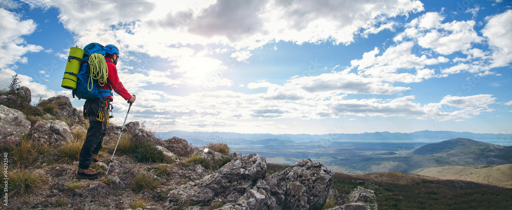 Obraz premium Panoramic photo of mountaineers standing with backpack on top of a mountain and enjoying the view