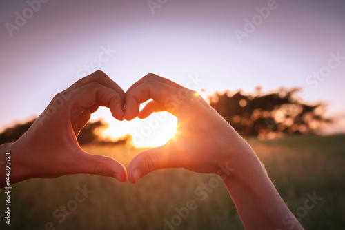 Hand shaped heart against sunset. 