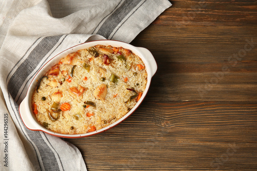 Baking dish with delicious rice and chicken on wooden table