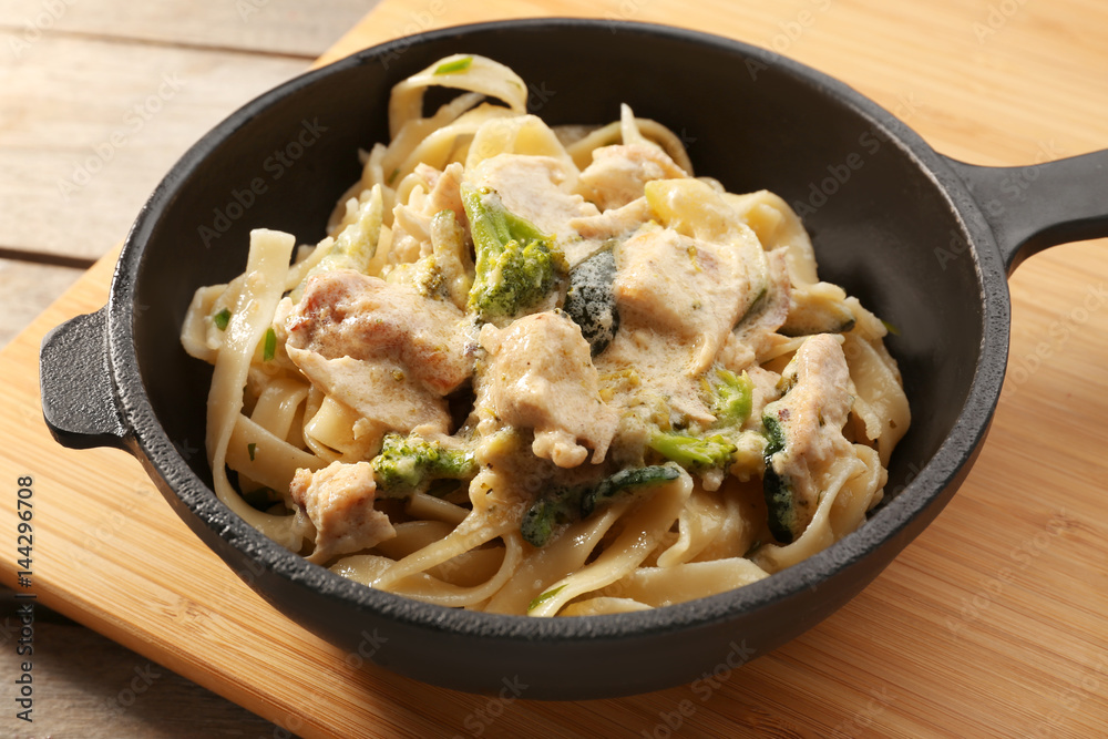 Frying pan with delicious chicken Alfredo on wooden board