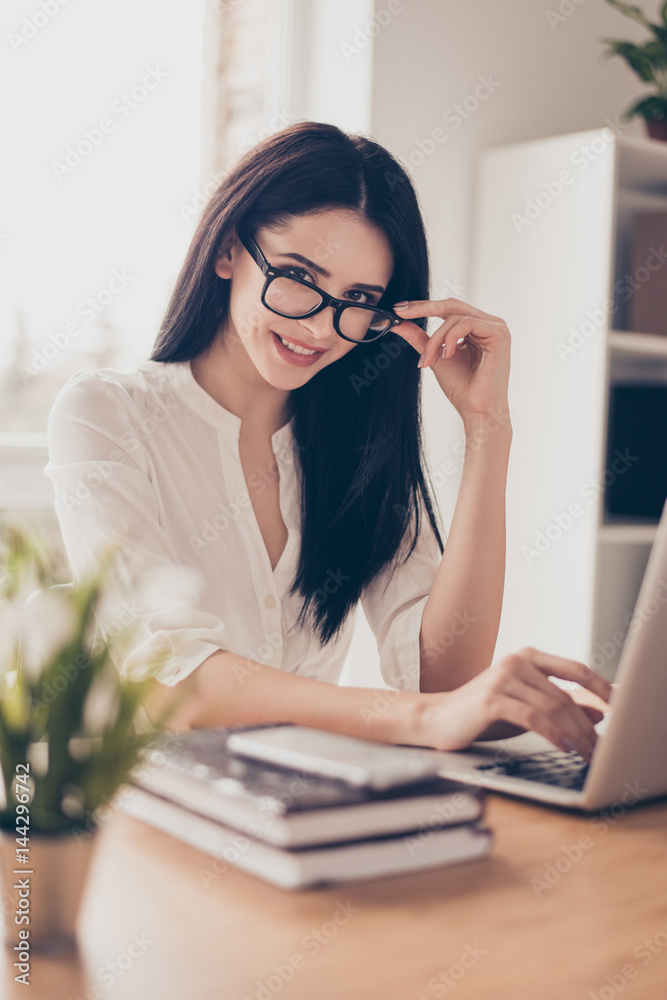 Portrait of cute young beautiful woman in glasses sits at a desk with a laptop and looks directly into the camera Portrait of cute young beautiful woman in glasses sits at a desk with a laptop and looks directly into the camera