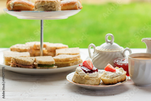 English afternoon teas in the garden cafe: scones with clotted cream and jam, strawberries, with various sadwiches on the background, selective focus