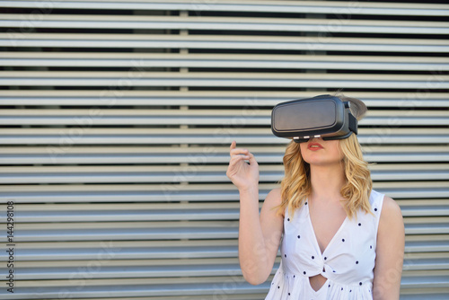 Happy young woman using a virtual reality glasses in a modern metal background