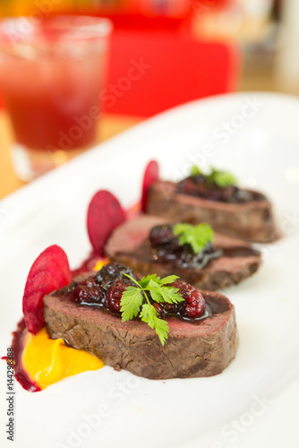 Organic Venison served with fresh raspberry raspberry sauce  beetroot slices and pumpkin puree  on a white plate.