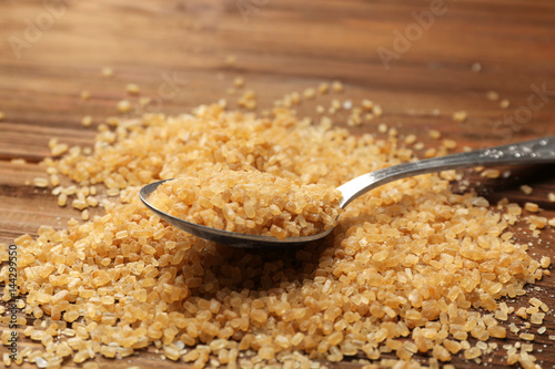 Heap of brown sugar and spoon on wooden background