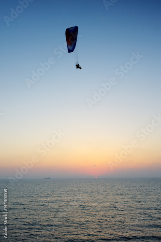Powered paraglider flying over the sea at sunset sky background