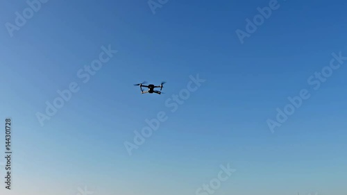 Unbemanntes Flugobjekt, auch Drohne genannt, fliegt am blauen Himmel über die Dächer photo