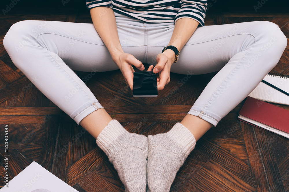 Cropped image of a girl in jeans sits at home on the floor and uses a smart phone