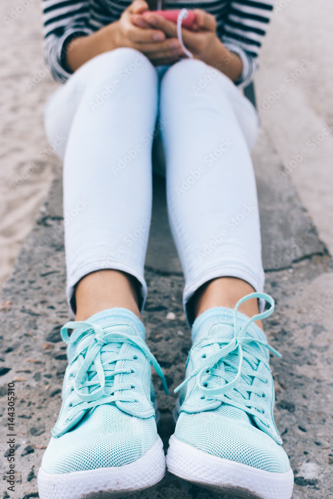 Vertical framing of female legs in jeans and sneakers.