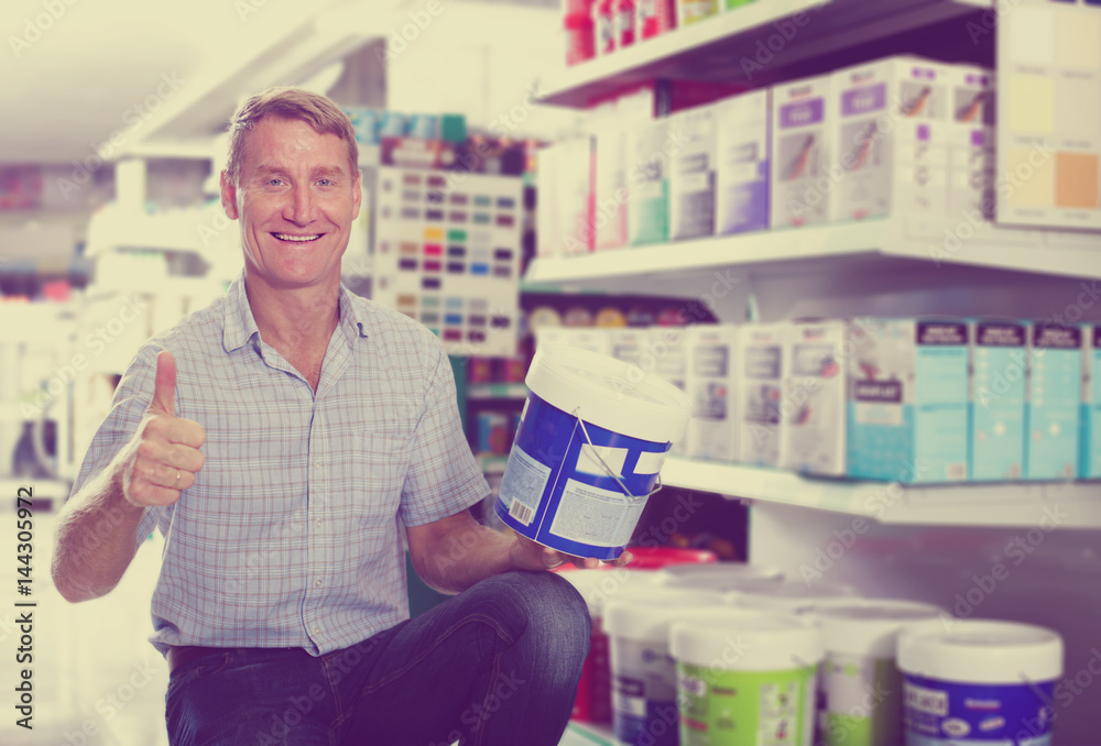 smiling man customer choosing paint bucket in hypermarket