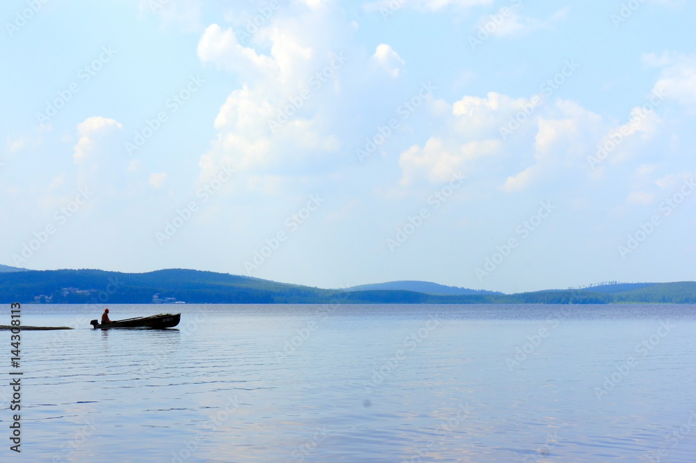 On a mountain lake a man sails on a boat in the summer evening