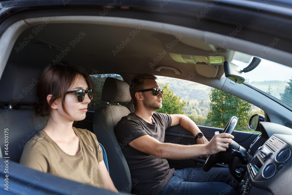 Young couple smiling, sitting in car, enjoying mountains view.