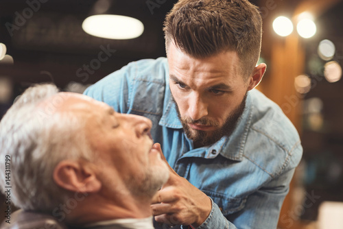 Peaceful barber styling beard of the old man in barbershop