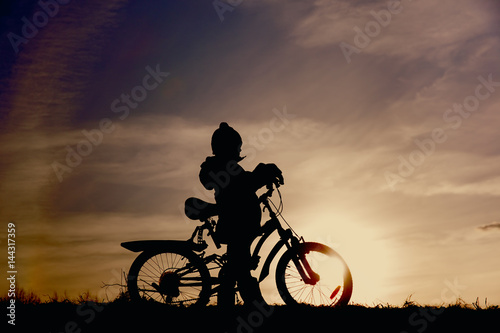 little boy riding bike at sunset sky