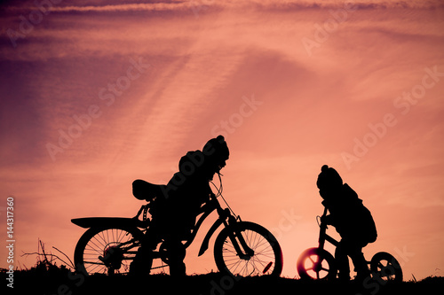 little boy and girl riding bikes at sunset sky