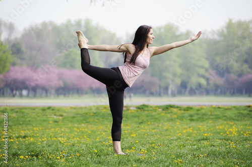 Young woman doing yoga in morning park. Standing half bow pose, utthita ardha dhanurasana. Healthy lifestyle outdoor conception. 