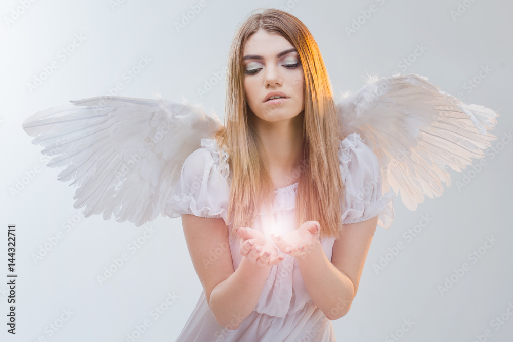 An angel from heaven holding light on the palms. Young, wonderful blonde girl in the image of an angel with white wings. An angel from heaven holding light on the palms. Young, wonderful blonde girl in the image of an angel with white wings.