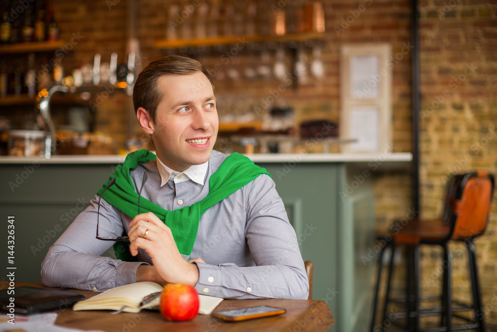Happy businessman sits at the table with working things and keeps glasses in his hand in time of a break, in a cafe Happy businessman sits at the table with working things and keeps glasses in his hand in time of a break, in a cafe