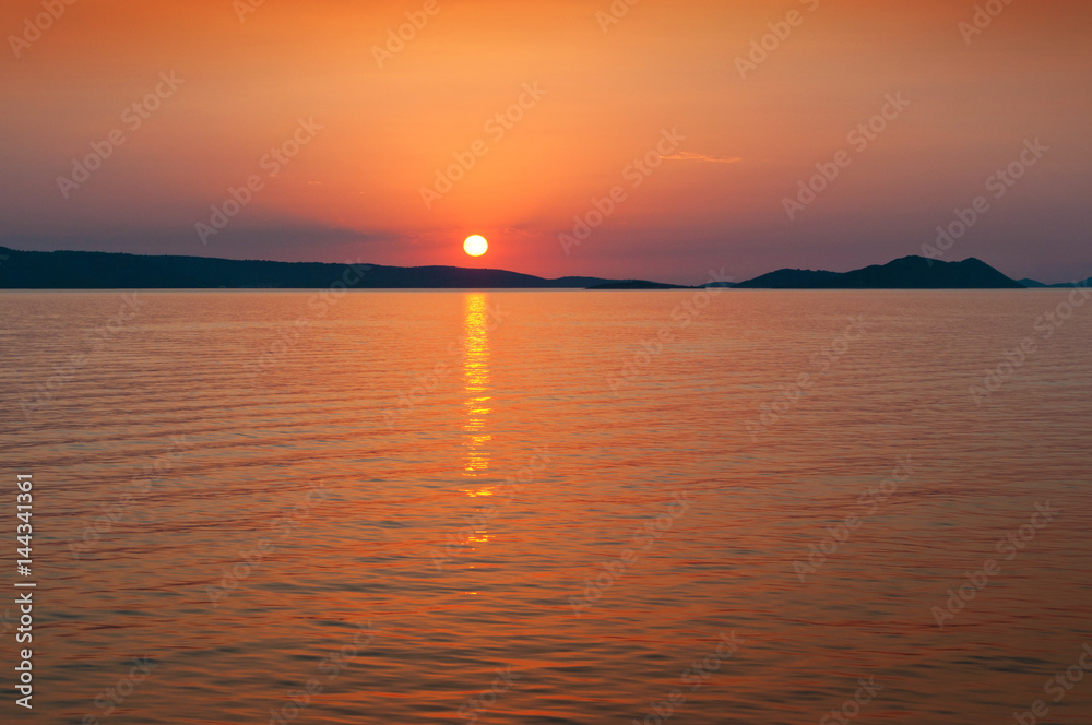 Sun setting above a hill range in the sea near the coast of Croatia. landscape in orange and red colors