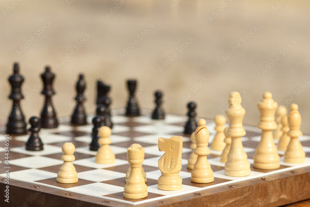 Close up wooden chess pieces on board, selective focus on white knight. Outdoors chess game Close up wooden chess pieces on board, selective focus on white knight. Outdoors chess game