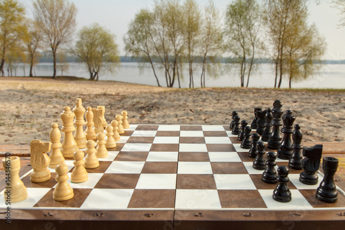 Chess board with chess pieces on river embankment background