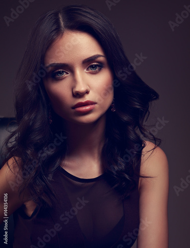 Sexy young makeup model in brown dress and curly hairstyle posing on dark shadow background. Closeup drama art toned portrait.
