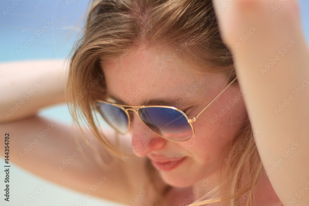 Femme portant des lunettes de soleil se recoiffant à la plage Femme portant des lunettes de soleil se recoiffant à la plage