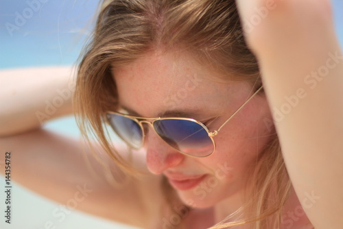 Femme portant des lunettes de soleil se recoiffant à la plage © Mathieu