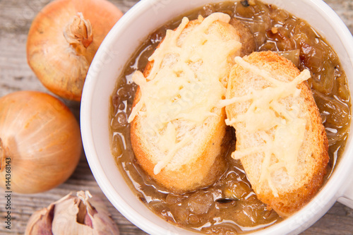 Onion soup with toast on a wooden background with some onions and garlic