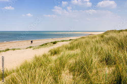 Fototapeta Naklejka Na Ścianę i Meble -  Two people with rucksacks walking down a sandy beach on a sunny day in Burnham Overy Staithe Norfolk England UK
