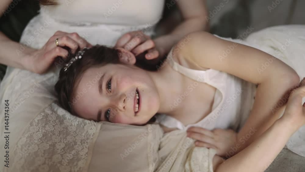 Mother and daughter hugging and cuddling in bed. Pretty little girl and beautiful woman lie together. Girls in lace dresses playing in decorated room. Family weekend, beauty day, having fun, love. Mother and daughter hugging and cuddling in bed. Pretty little girl and beautiful woman lie together. Girls in lace dresses playing in decorated room. Family weekend, beauty day, having fun, love.