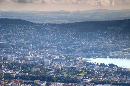 Cityscape of Zurich, colorful rooftops and spires of the old town with Lake Zurich, green forested hills and mountains in the background, seen from Uetliberg, Switzerland, Europe.