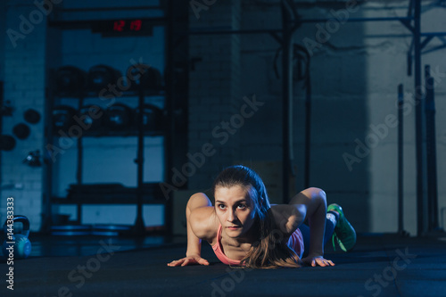 Fit woman in colourful sportswear doing burpees on a exercise mat in a grungy industrial type space