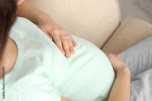 Beautiful pregnant woman sitting on sofa at home, closeup