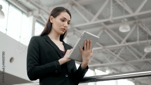 Attractive businesswoman using a digital tablet while standing in front of windows in an office building overlooking the city, young enterpreteur freelancer. photo