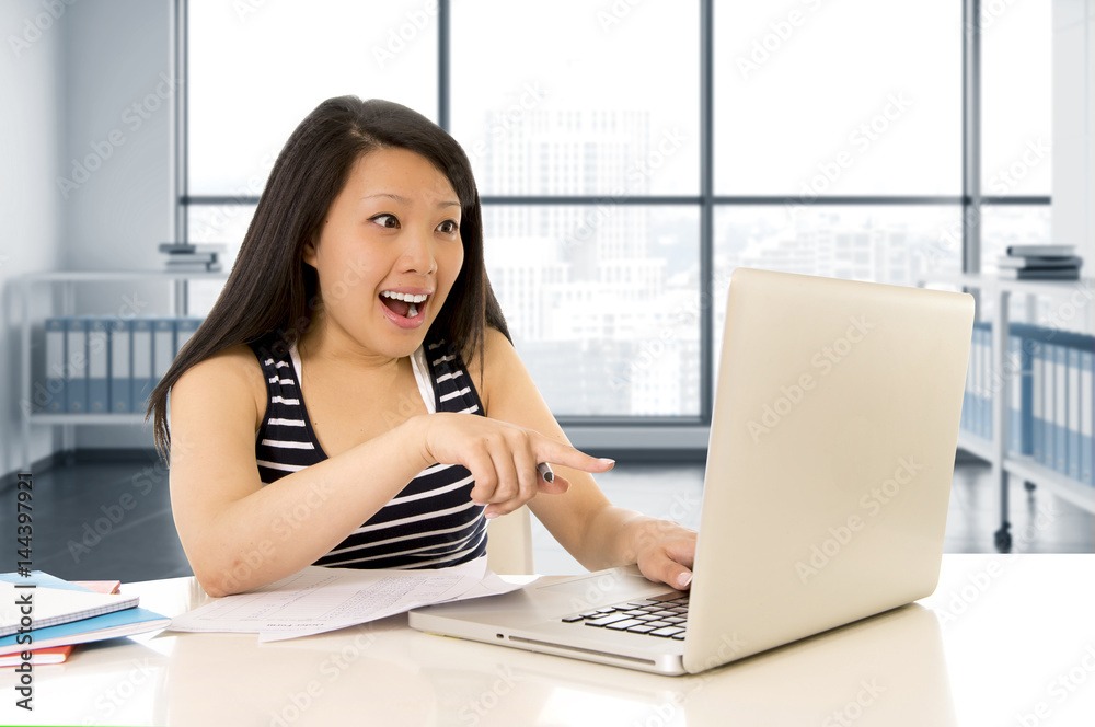 happy chinese asian woman working and studying on her computer sitting at modern office desk smiling cheerful
