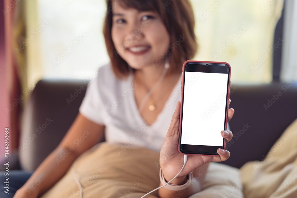 Asian woman showing at blank screen smart phone on sofa in living room in selective focus.