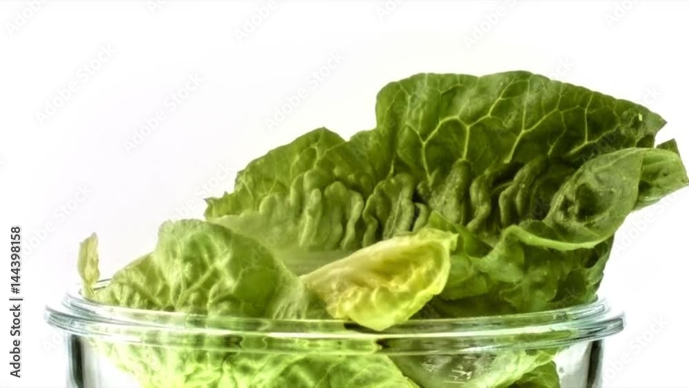 Feuille de salade qui tombe dans un bol en verre de salade en slow motion gros plan