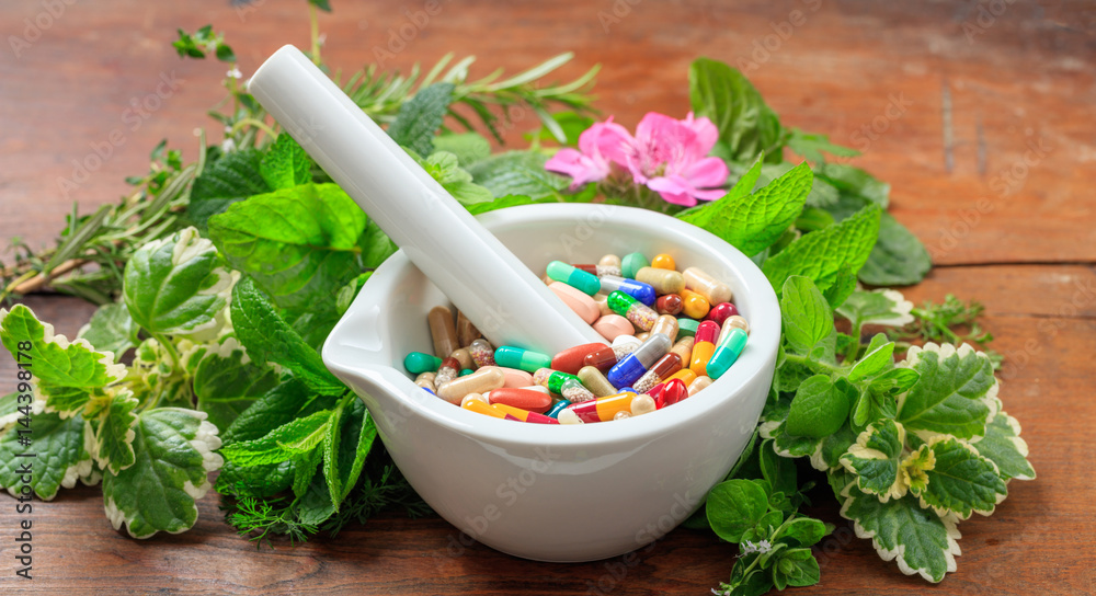 Alternative medicine concept - Herbs and pills in a mortar on wooden background