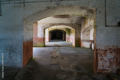 Masonry arched hallway stretching away into the darkness. Typical of forts and prisons of the Victorian period