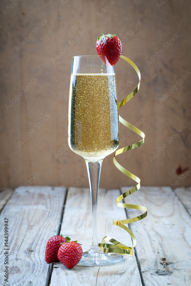 champagne sparkling white wine glass and bottle on plain background with strawberry garnish gold ribbon