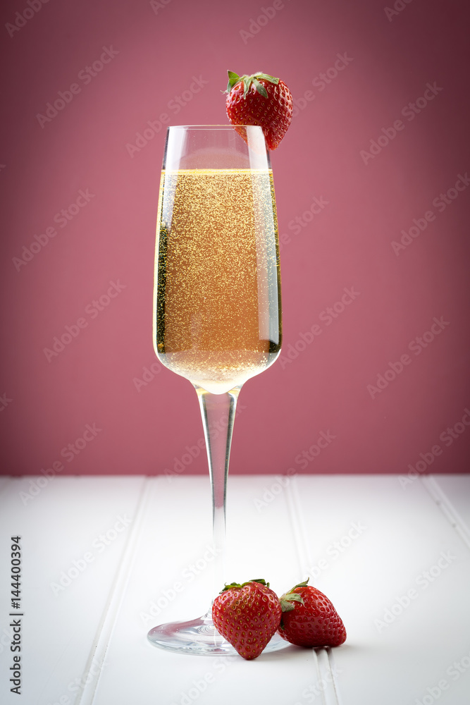 champagne sparkling white wine glass and bottle on plain background with strawberry garnish gold ribbon